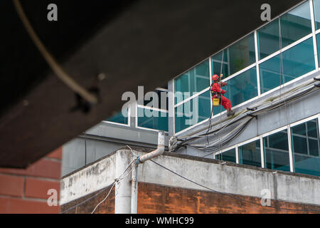 DENPASAR/Bali, Indonesien - 26. AUGUST 2019: Hausmeister oder Reinigung Service waren die Reinigung der Fenster befindet sich auf der Höhe eines mit kompletten safet Gebäude Stockfoto