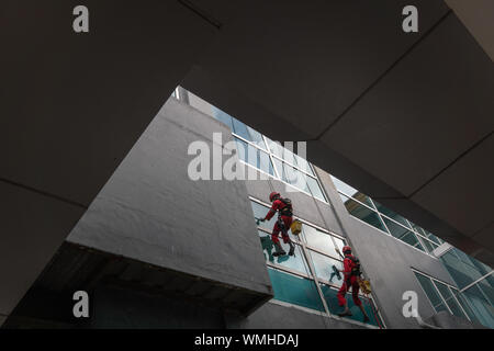 DENPASAR/Bali, Indonesien - 26. AUGUST 2019: Hausmeister oder Reinigung Service waren die Reinigung der Fenster befindet sich auf der Höhe eines mit kompletten safet Gebäude Stockfoto