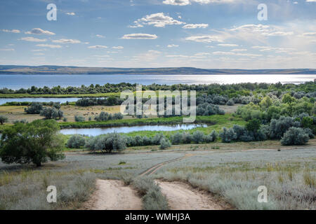 Blick auf eine Breite, Volle fließenden Fluss mit Sun Flair auf den bewaldeten Ufern und Wolken im blauen Himmel. Wolga. Stockfoto