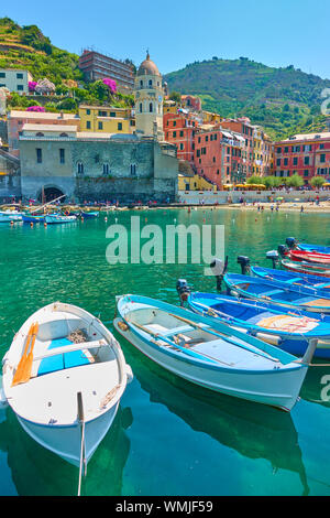 Boote im Hafen und Uferpromenade mit Gebäuden, die durch das Meer in Vernazza Stadt auf sonnigen Sommertag, Cinque Terre, Italien Stockfoto