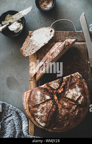 Brot und Butter Frühstück oder einen Snack. Flachbild-lay von frisch gebackenem Sauerteigbrot Laib und Schichten mit Butter und geräuchertes Salz über grauer Beton Tabelle ba Stockfoto