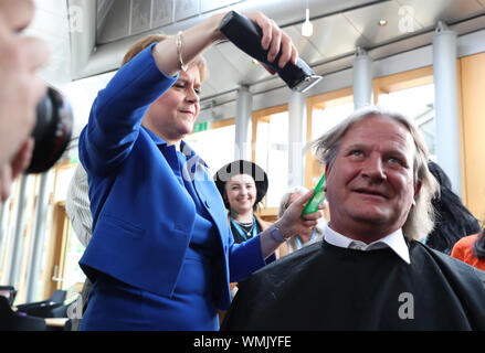 Erster Minister Nicola Sturgeon schneidet die Haare von David Torrance MSP Anheben £ 1000 für die Nächstenliebe Maggie's Center in Kirkcaldy an der schottischen Parlament in Edinburgh. Stockfoto