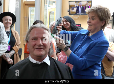 Erster Minister Nicola Sturgeon schneidet die Haare von David Torrance MSP Anheben £ 1000 für die Nächstenliebe Maggie's Center in Kirkcaldy an der schottischen Parlament in Edinburgh. Stockfoto