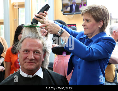 Erster Minister Nicola Sturgeon schneidet die Haare von David Torrance MSP Anheben £ 1000 für die Nächstenliebe Maggie's Center in Kirkcaldy an der schottischen Parlament in Edinburgh. Stockfoto