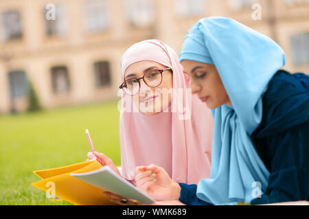 Frau in Blau hijab lächelnd während des Studiums mit Freund Stockfoto