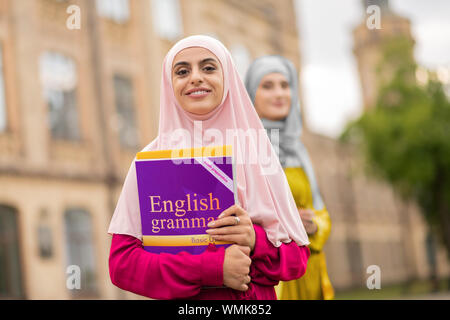 Schönen muslimischen Student trägt Rosa hijab Holding Buch Stockfoto