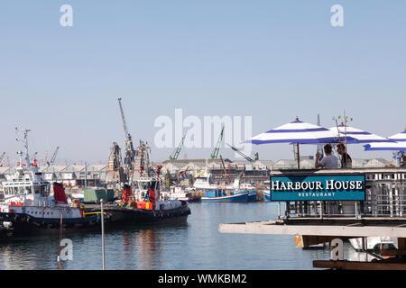 Menschen essen im Harbor House Restaurant mit Blick auf die kommerzielle Schifffahrt im Hafen an der V&A Waterfront, Kapstadt, Südafrika Stockfoto