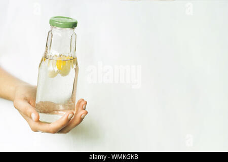 Glas Flasche mit Wasser und Zitrone in weiblicher Hand. Das Thema der Bedeutung von Trinkwasser Ihre täglichen Flüssigkeitsaufnahme. Gesunder Lebensstil, null Abfall-, Kunststoff-, Eco-friendly Shopping, vegan Stockfoto