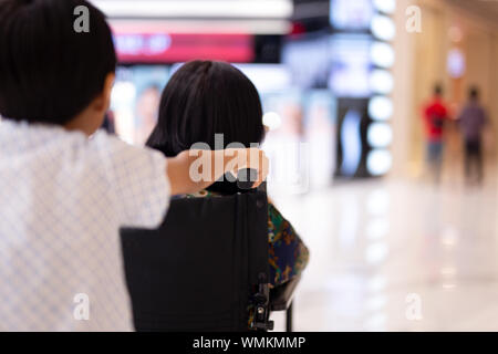 Jungen drücken Urgroßmutter im Rollstuhl bei Shopping certer. Stockfoto