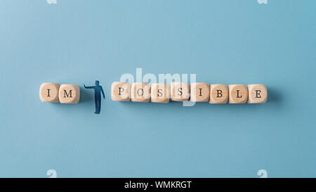 In der breiten Ansicht Bild einer Silhouette mann abbildung wegdrücken Buchstaben im von Das Wort unmöglich geschrieben auf Holz Würfel. Über blauen Hintergrund. Stockfoto