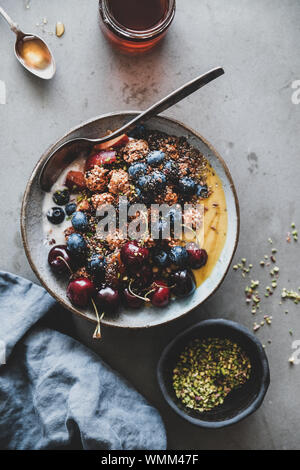 Gesundes Frühstück. Flachbild-lay von Quinoa Hafer Müsli coconut Joghurt Schale mit frischem Obst, Honig, Samen, Nüsse, Beeren über grauer Beton Tabelle backgroun Stockfoto