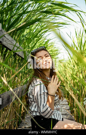 Schöne Mädchen mit einem gestreiften Hemd, sitzen auf einem Holz weg, lächelnd und eine gute Zeit haben, am Schilf National Reservation, Sic-Dorf, Romani Stockfoto