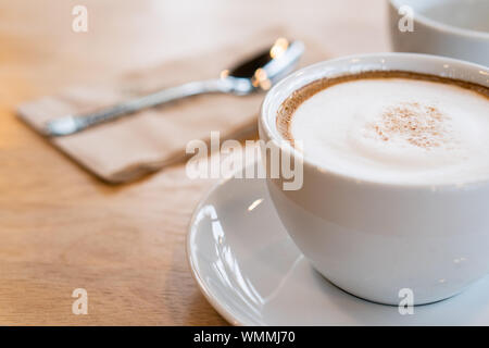 Heißer Kaffee, weiße Tassen, Teller, Löffel und Gewebe alle auf dem Holztisch. Stockfoto
