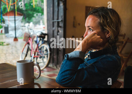 Nachdenkliche Frau sitzend genießen eine Tasse Kaffee an regnerischen Tag Stockfoto
