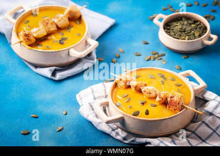 Hausgemachte Herbst essen mit Kürbis creme Suppe in Schalen mit Saatgut und Fleischspieße. Lecker Kürbis Teller auf blauem Hintergrund. Thanksgiving Suppenschüsseln. Stockfoto