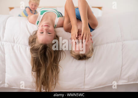 Schwester und Bruder spielen, lachen und den Kopf nach unten auf das Bett Stockfoto