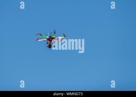 Quadrocopter mit einer Video kamera fliegt in den klaren blauen Himmel. Die sichtbaren Teile der Geräte, Kabel, Propellerflügel drehen. Multi-gefärbt. Kopieren Sie Platz. Stockfoto