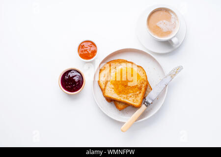 Morgen Toast mit Butter und Marmelade auf weißen Tisch mit einer Tasse Kaffee mit Milch. Ansicht von oben, flatlay Stockfoto