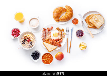 Ansicht von oben flatlay mit Sorten von frischem Frühstück: Spiegeleier mit Speck und Würstchen, Müsli mit Beeren, gebratene Toast mit Marmelade und Butter. Weiß Stockfoto