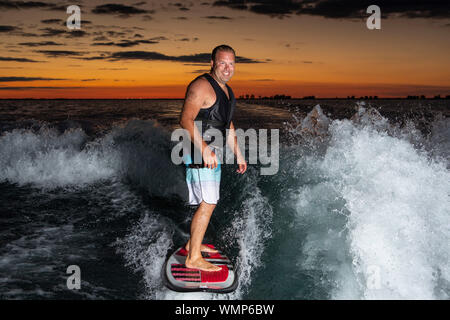 Ein Mann Surfen auf einem Boot wake kurz nach Sonnenuntergang. Stockfoto