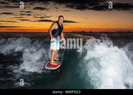 Ein Mann Surfen auf einem Boot wake kurz nach Sonnenuntergang. Stockfoto