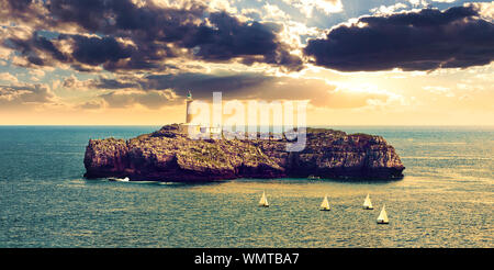 Leuchtturm auf dem Meer über den Felsen in Kantabrien, Santander, Spanien.Seascape von Sonnenuntergang und herrlichem Himmel. Boote, die im Meer segeln Stockfoto