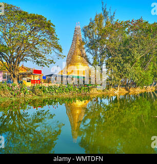 Die Ausbreitung der grünen Bäume und Golden Shwe Baww Di Pagode sind auf spiegelfläche von Tharzi Teich, Nyaungshwe, Myanmar wider Stockfoto