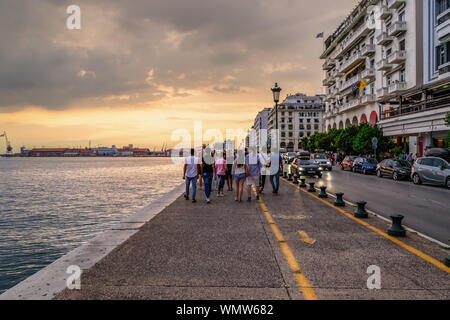 Thessaloniki, Griechenland Masse an historischen Waterfront. Die Menschen laufen Sie entlang der Promenade Richtung Hafen der Stadt am Goldenen Stunde mit vorbeifahrenden Autos an Nikis Avenue. Stockfoto