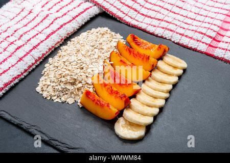 Haferflocken in Scheiben geschnitten Nektarinen und Bananenscheiben auf schwarzem Schiefer Fach verfeinert. Die Alternative gesünderes Frühstück Frühstück aber vielleicht schwer zu Durch af kommen Stockfoto