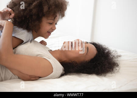 Gerne schwarze Mutter lag auf dem Bett, Holding glücklich süße Tochter. Stockfoto