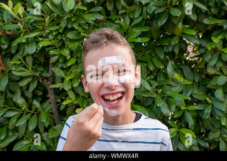 Junge mit Gips auf seinem Gesicht vor einem Hedge lachen Stockfoto