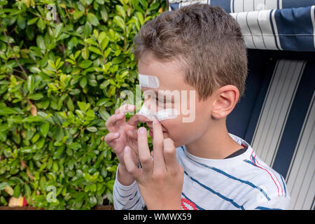 Junge mit Gips auf seinem Gesicht vor einem Hedge lachen Stockfoto