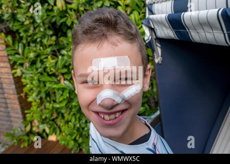 Junge mit Gips auf seinem Gesicht vor einem Hedge lachen Stockfoto