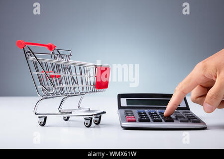 In der Nähe von Leer Warenkorb in der Nähe der Person Hand mit Taschenrechner über Weiß Schreibtisch Stockfoto