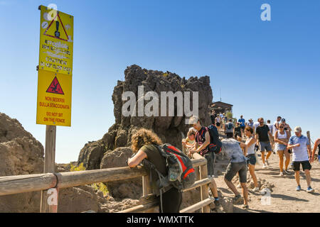 Neapel, Italien - AUGUST 2019: Menschen auf dem Pfad um den Krater des Vesuv am Stadtrand von Neapel. Im Vordergrund ist ein Warnzeichen. Stockfoto