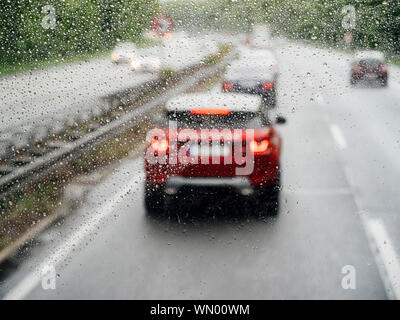 Erhöhten Blick auf die Vorderseite der roten Auto durch die mit Regentropfen Windschutzscheibe von Bus Bus oder Lkw abgedeckt Stockfoto