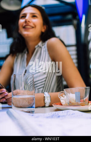 Junge Brünette an ihrem Schreibtisch mit Unterlagen und mobiles Arbeiten. Geschäftsfrau arbeiten an Schreibarbeit Stockfoto