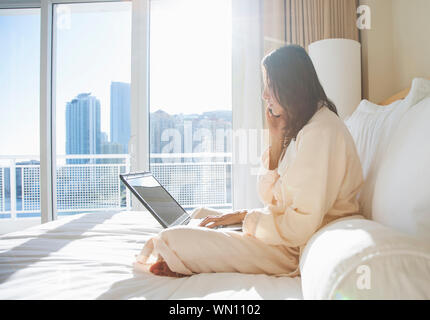 Frau mit Bademantel mit Laptop während Anruf Stockfoto