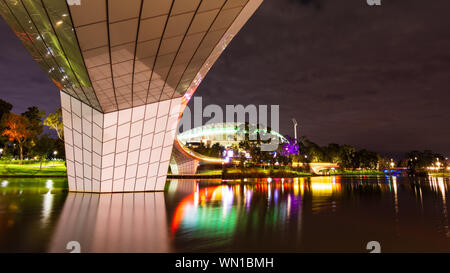 Der Fluss Torrens Fußgängerbrücke durch die Nacht, mit Adelaide Oval Sports Arena im Hintergrund. Adelaide Australien. Stockfoto