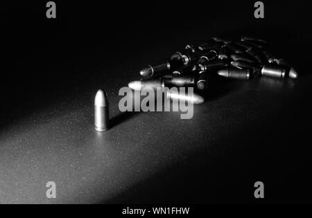 Eine einzelne 9mm bullet steht allein mit starken seitlichen Licht erzeugen lange Schatten mit einem Stapel von Kugeln im Hintergrund in Schwarz und whtie Stockfoto