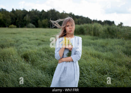 Windswept Frau mit gelben Blumen im Feld Stockfoto