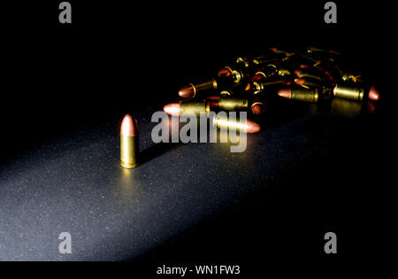 Eine einzelne 9mm bullet steht allein mit starken seitlichen Licht erzeugen intensive Farbe mit einem Stapel von Kugeln hinter im Schatten Stockfoto