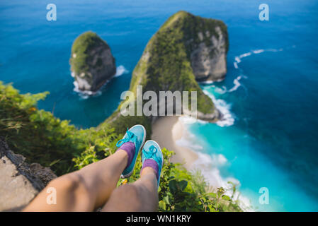 Die Beine der Frau oben Kelingking Strand in Nusa Penida, Indonesien sitzen Stockfoto