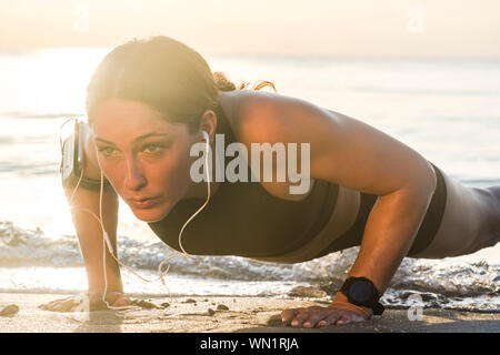 Frau mit Kopfhörern push-up am Strand Stockfoto