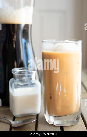 Ein Glas mit kaltem Kaffee brühen mit Sahne und Eis in der Nähe der Krug auf einem Küchentisch gefüllt Stockfoto