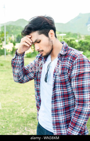 Jungen asiatischen Menschen Gefühl ernstes Gesicht ist weg schauen beim Stehen draußen allein auf die Natur Herbst Tag. Mann mit bärtigen hipster Kerl emotion Konzept. Stockfoto