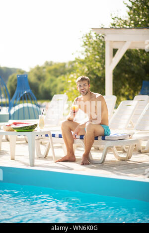 Stattlicher Mann mit heißem Wetter während Chillen in der Nähe von Pool Stockfoto