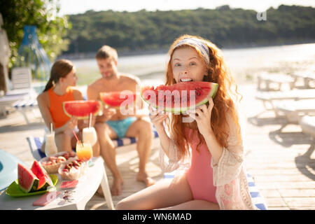 Rothaarige Frau, die lustiges Gesicht beim Beißen Wassermelone Stockfoto