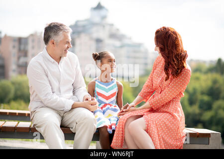 Glückliche Familie sitzt auf der Bank bei einem Spaziergang in der Stadt Stockfoto