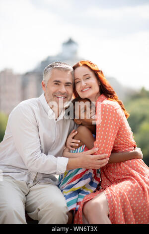 Mutter und Vater umarmt ihren niedlichen glückliche Tochter Stockfoto